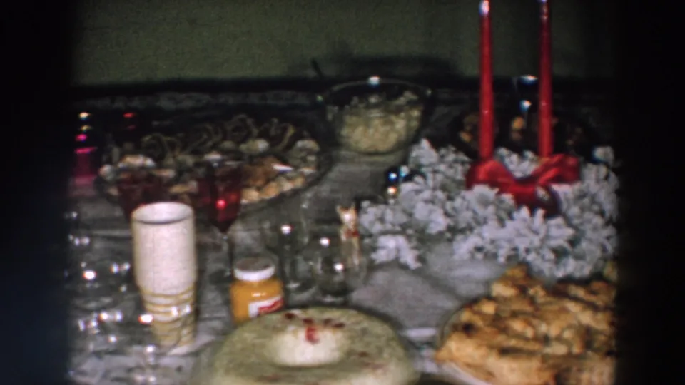 Soft 8mm frame from 1957 Wheeling, Ohio showing a festive table with cake, pastries, red candles, frosted wreath decor, cups, and glassware.
