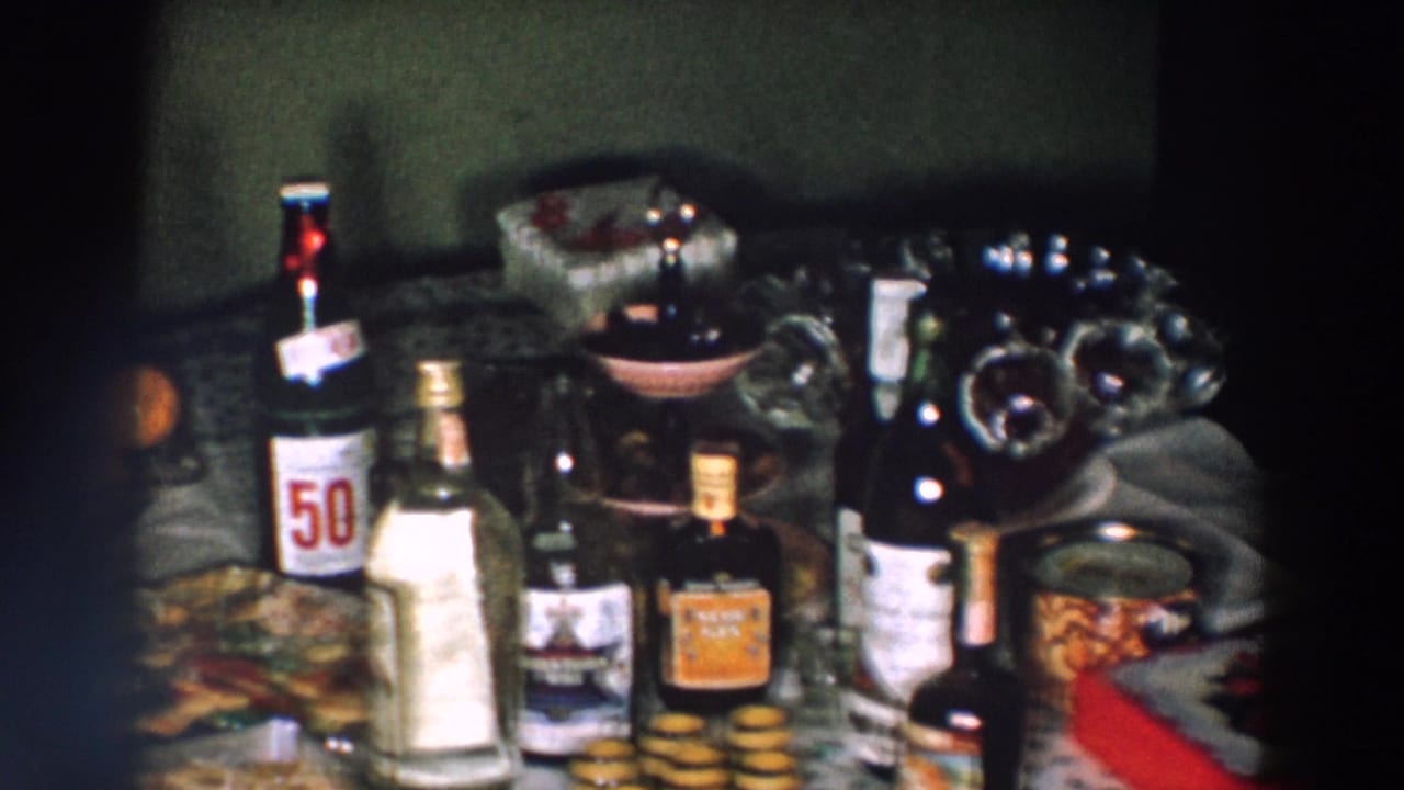 1957 Wheeling, Ohio frame of a crowded celebration table with 50/50 soda, assorted bottles, a bowl, food, and oranges.