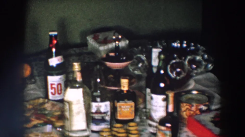 1957 Wheeling, Ohio frame of a crowded celebration table with 50/50 soda, assorted bottles, a bowl, food, and oranges.