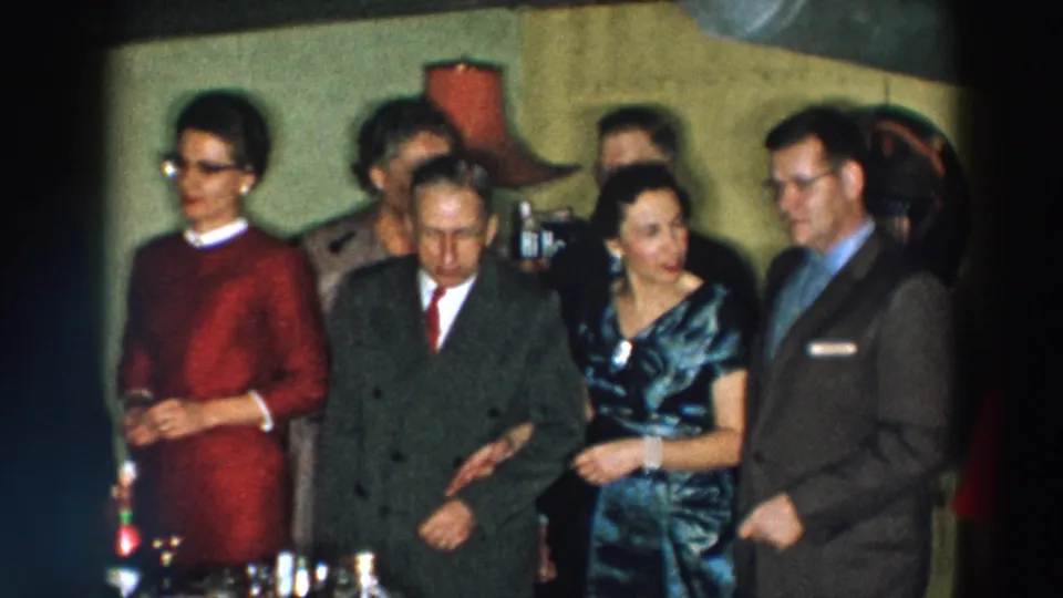 1957 Wheeling, Ohio frame showing women in formal dresses and men in suits gathered near a table with drinks.