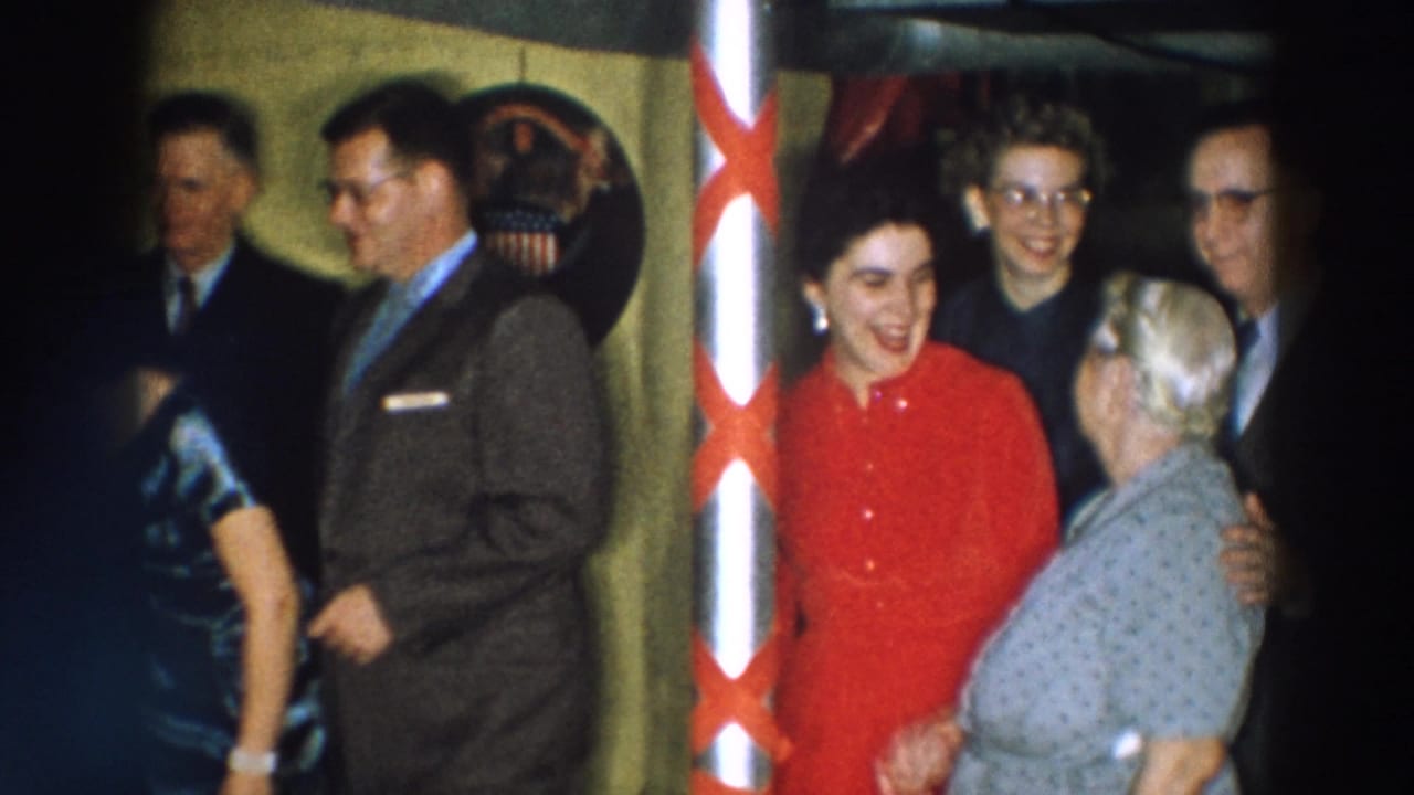 In Wheeling, Ohio home-movie footage from 1957, a woman in a red dress stands near a decorated pole with several adults around her.