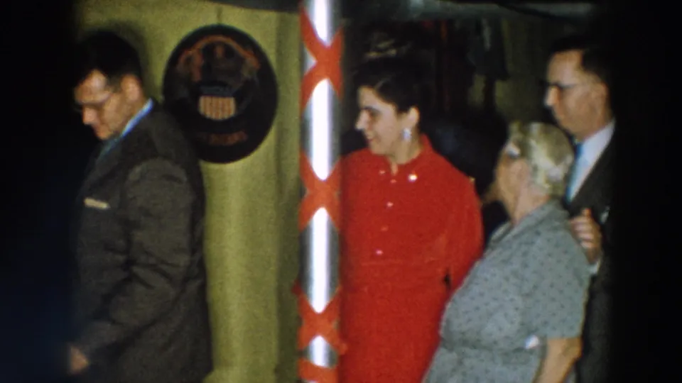 The final 1957 Wheeling, Ohio frame shows a woman in red and an older woman near a white pole with red ribbons and a circular wall emblem.
