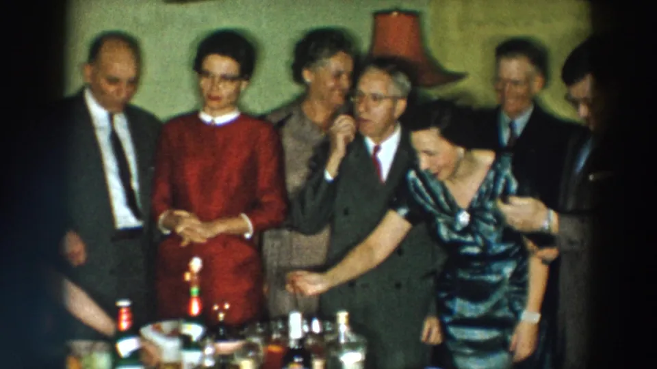 1957 Wheeling, Ohio home-movie frame of adults socializing in a private interior with drinks on a table.