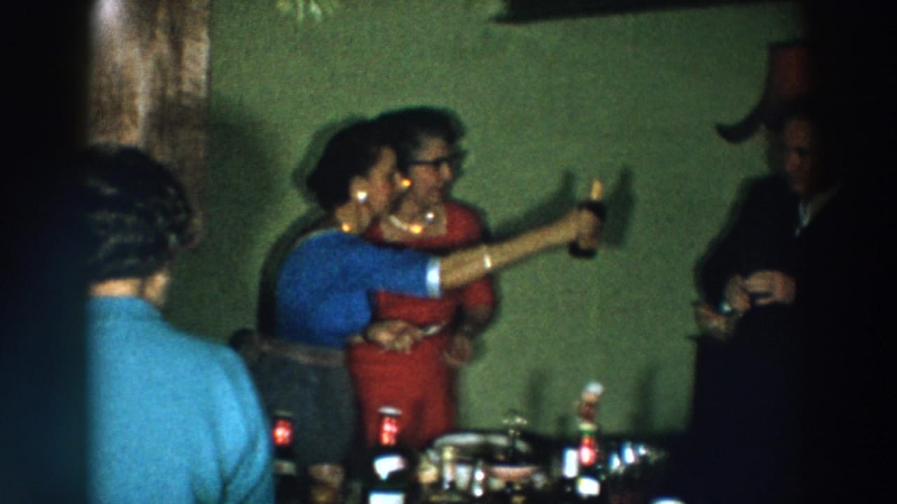 1957 Wheeling, Ohio home-movie frame showing party guests in suits and dresses raising drinks near a table.