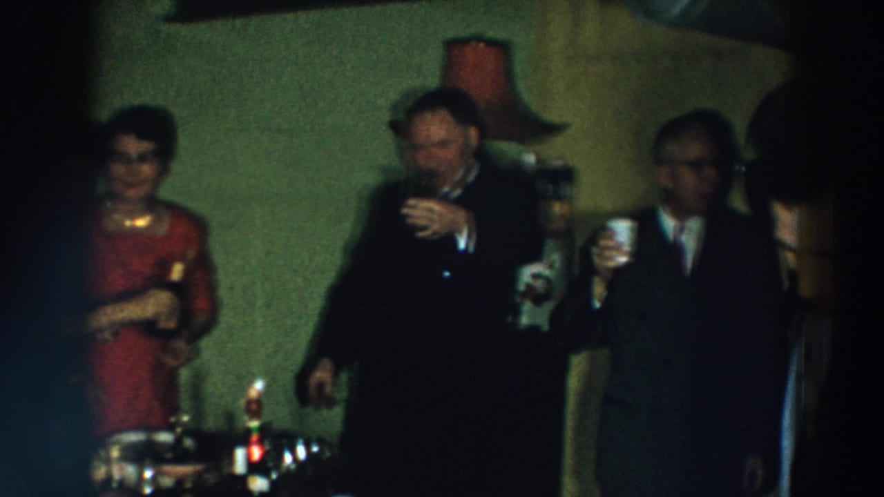 Party guests stand near a table with drinks as several people hold glasses.
