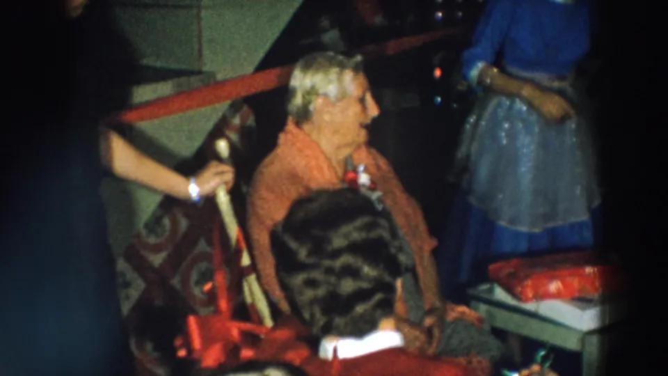 The birthday honoree sits beside wrapped presents while nearby guests stand and look on in the dim Wheeling, Ohio interior.