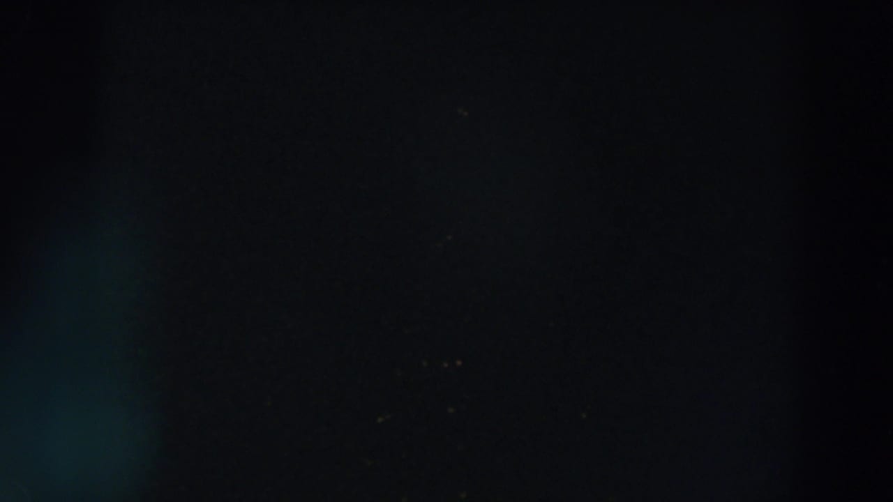 A very dark 1957 8mm frame from Wheeling, Ohio with a faint vertical form and small warm lights in the distance.