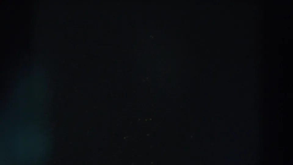 A very dark 1957 8mm frame from Wheeling, Ohio with a faint vertical form and small warm lights in the distance.