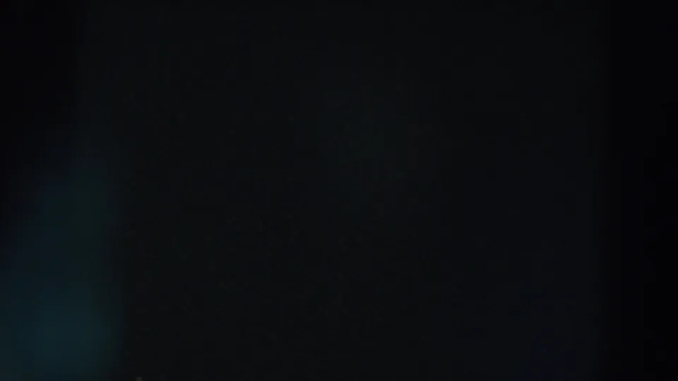 Underexposed 8mm night frame from the Wheeling, Ohio clip, with faint blue-green flare and obscured urban forms.