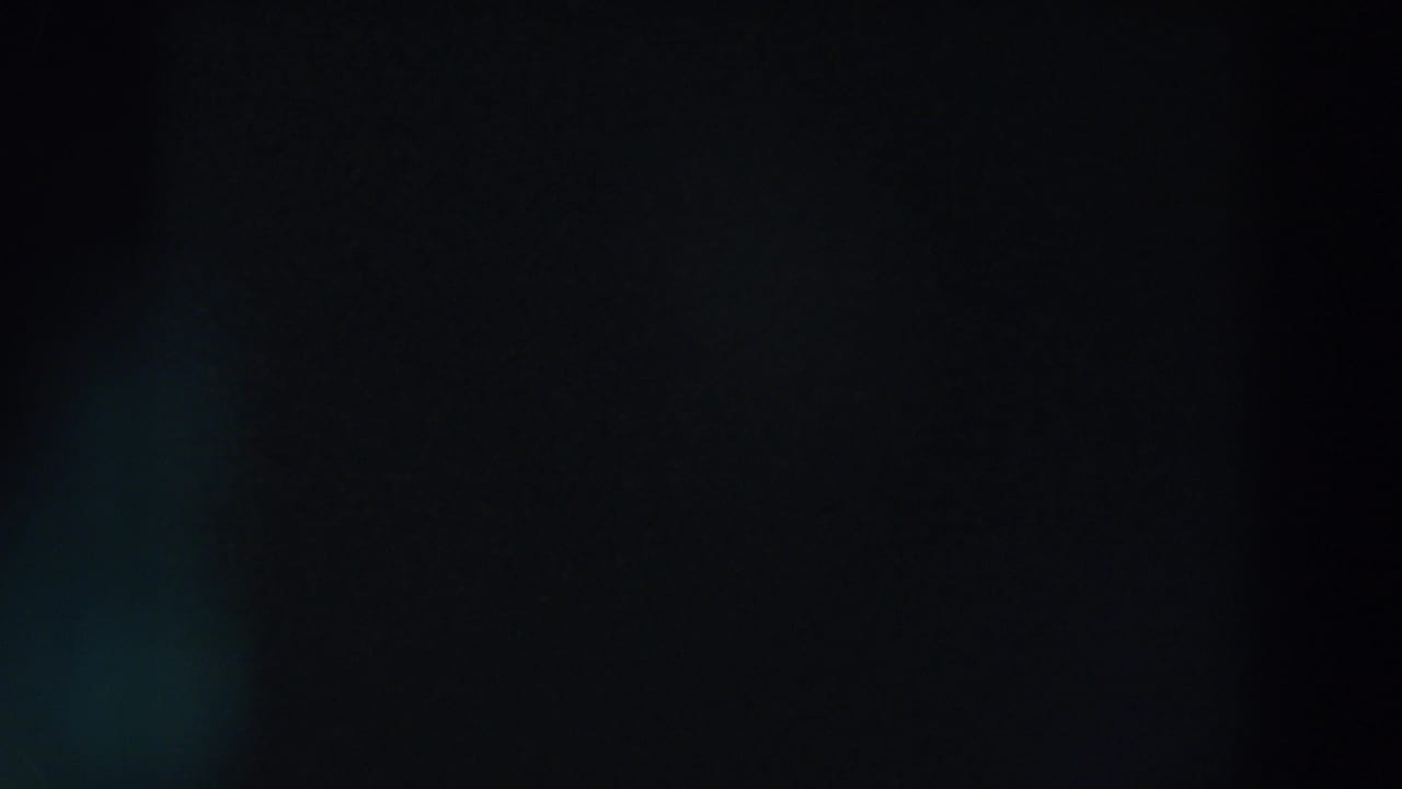 1957 Wheeling, Ohio 8mm frame showing near-total darkness with a soft blue-green lens flare and barely visible distant light.