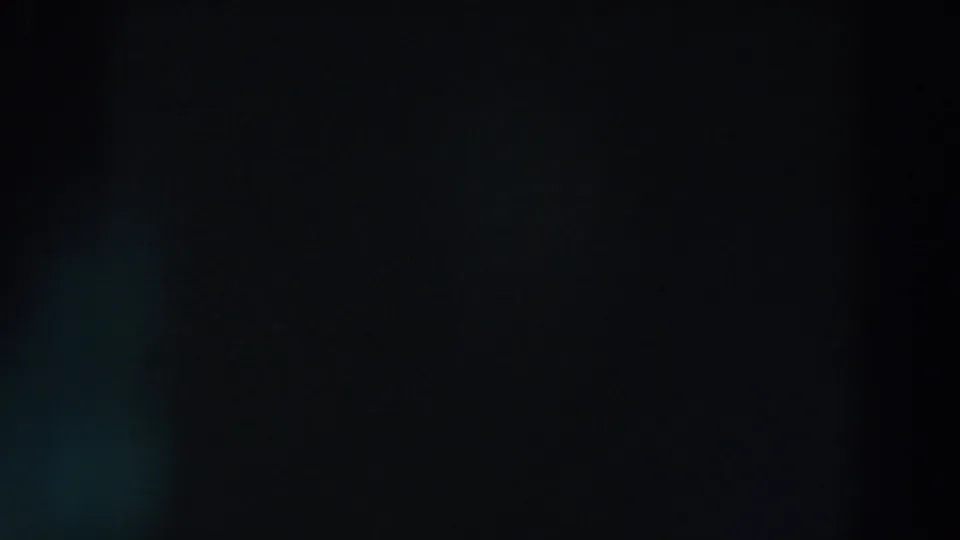 1957 Wheeling, Ohio 8mm frame showing near-total darkness with a soft blue-green lens flare and barely visible distant light.
