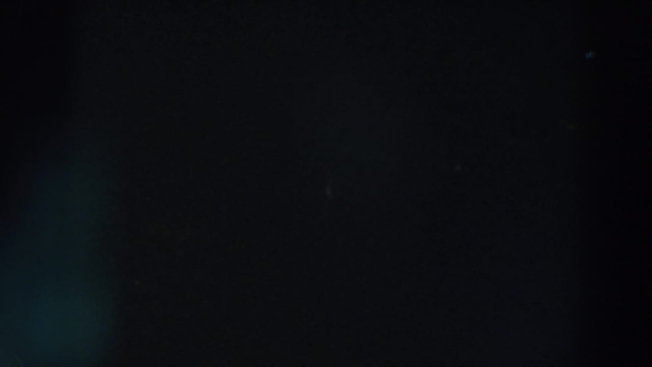 Mostly black night frame with dim colored lights near the upper left.