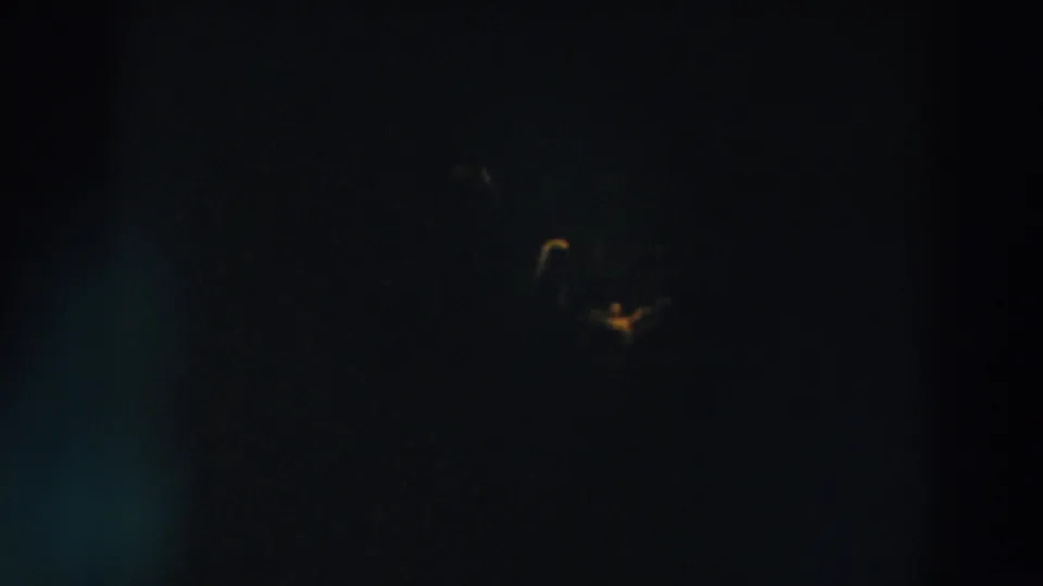 1957 8mm frame with faint distant lights, deep shadow, and a small curved yellow glow near the bottom.