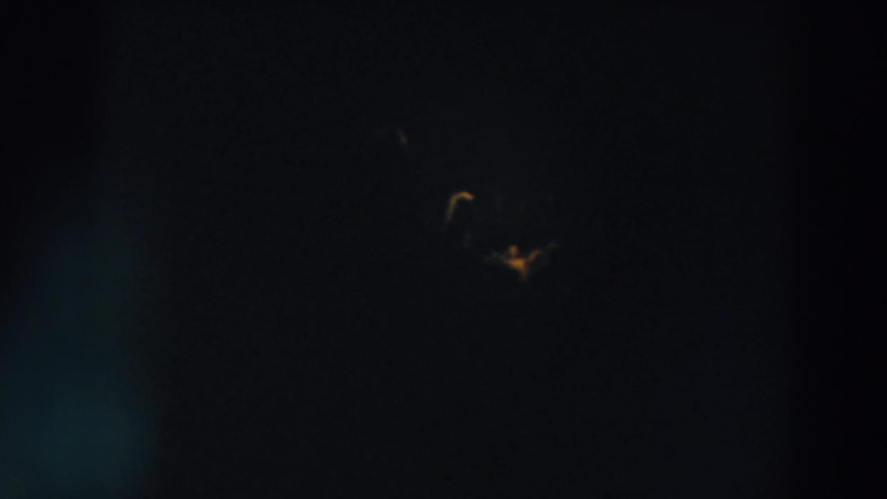 Very dark night sky with a small yellow light and faint colored specks.