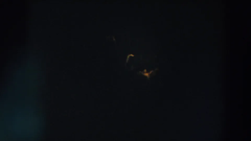 1957 Wheeling, Ohio home-movie frame showing a distant yellow antenna light in a nearly black night sky with faint film specks.