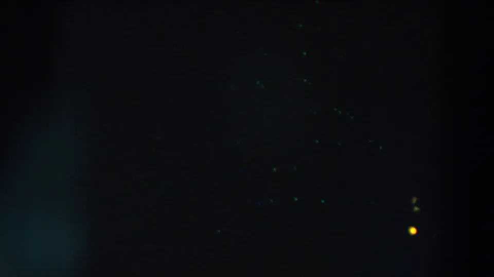 1957 home-movie frame with scattered green-blue specks and a small yellow light visible in the dark Wheeling night scene.