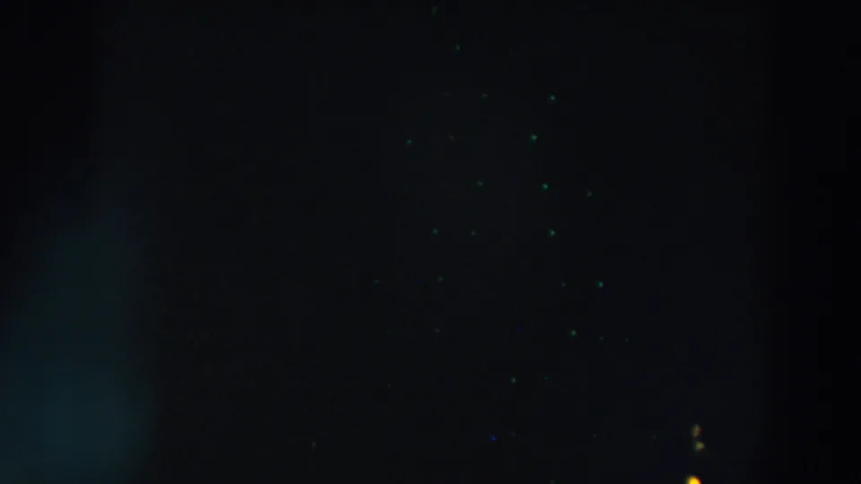 1957 8mm night frame from Wheeling, Ohio with faint green specks, soft blue-green flare, and heavy underexposure.