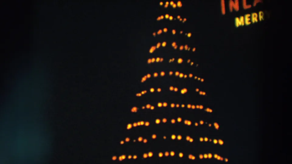 A bright bulb-lit Christmas tree dominates the final Wheeling night frame, with partial neon lettering at right.