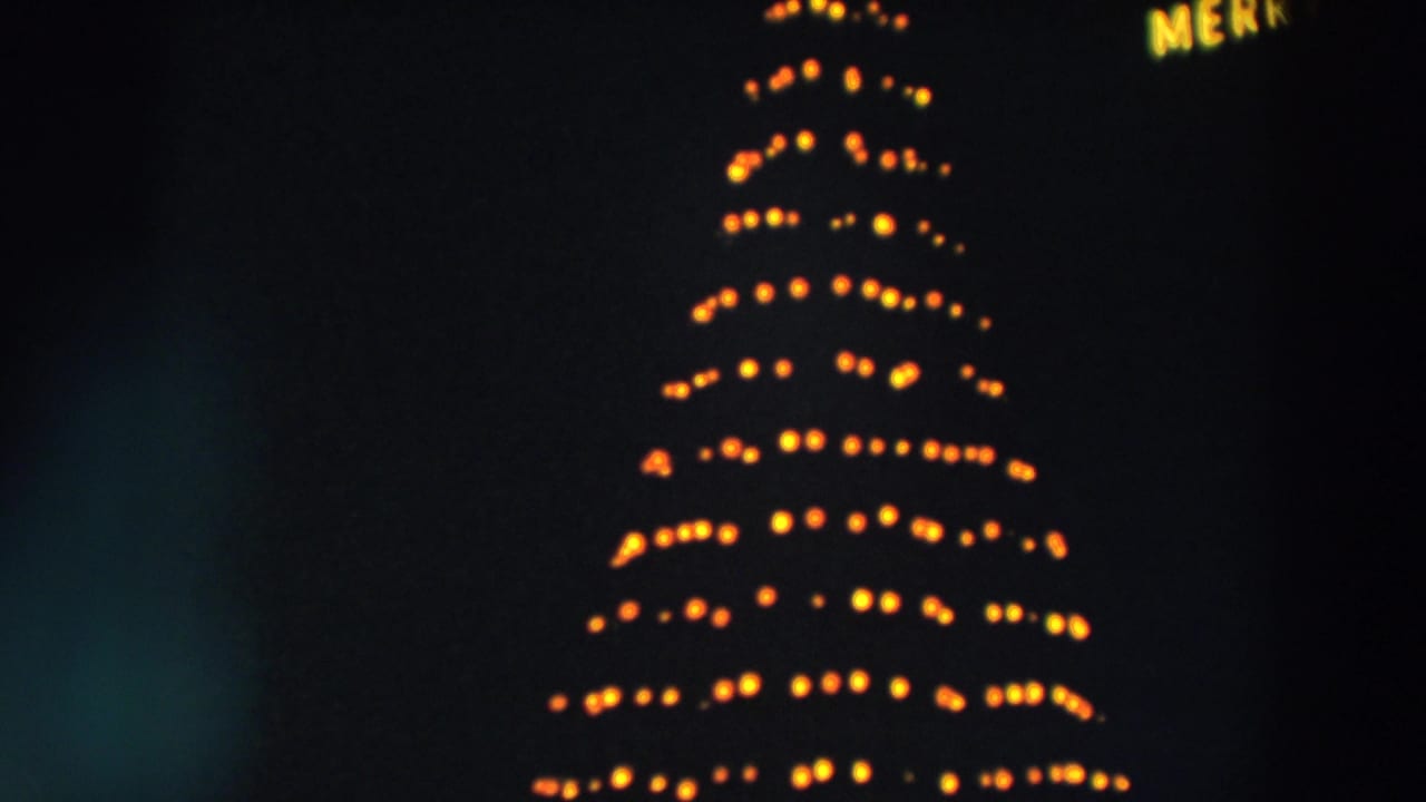 1957 Wheeling, Ohio 8mm frame showing warm yellow revolving Christmas tree lights at night with soft blur.
