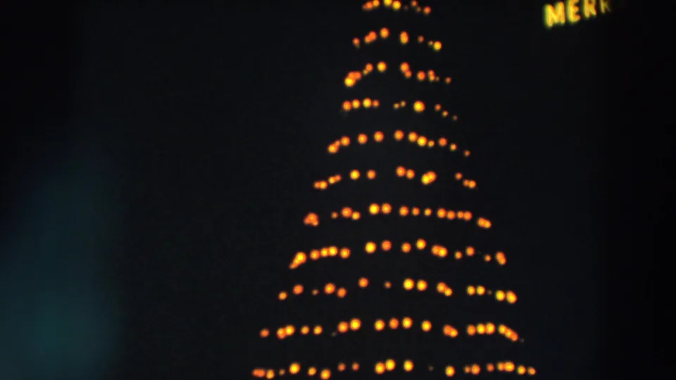 1957 Wheeling, Ohio 8mm frame showing warm yellow revolving Christmas tree lights at night with soft blur.