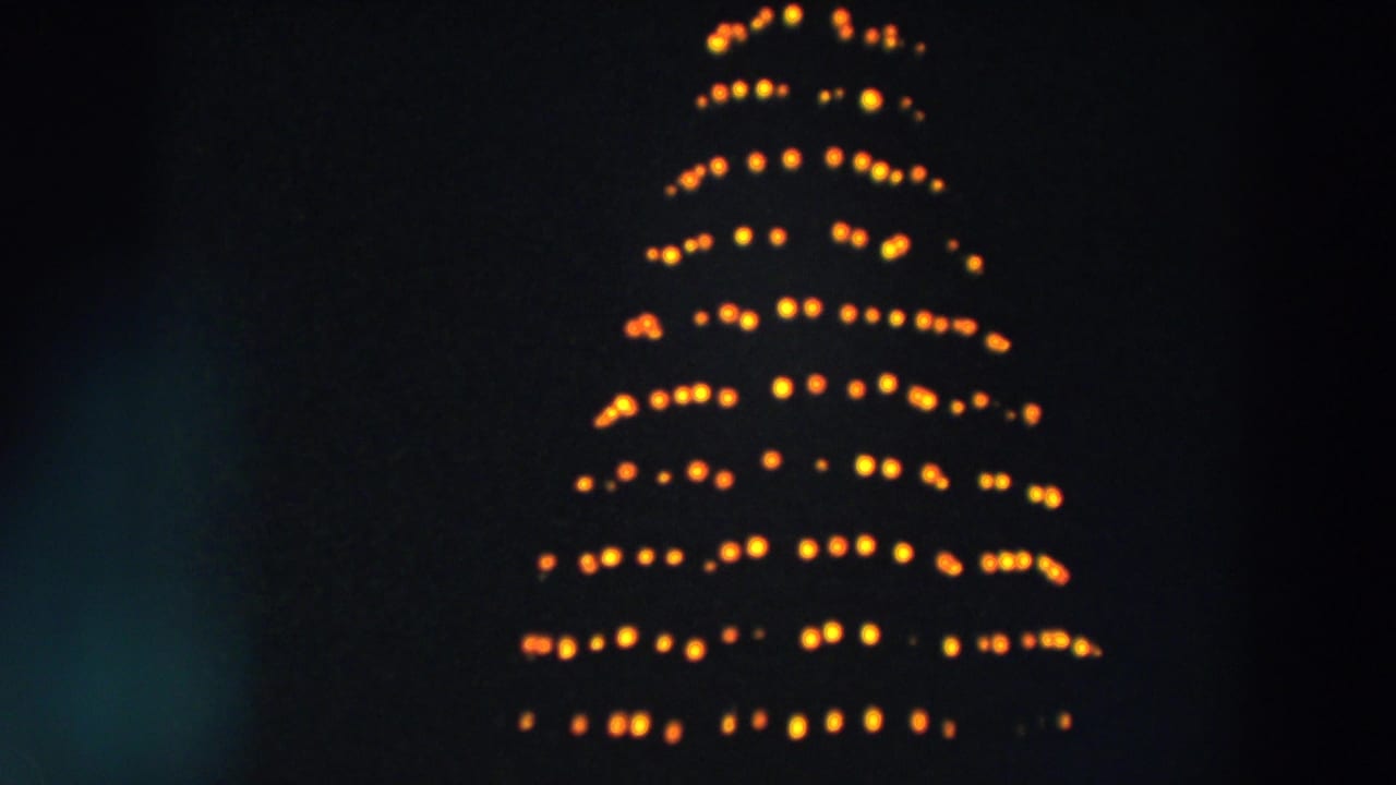 Yellow holiday lights form a conical tree shape beneath partial MERRY lettering.