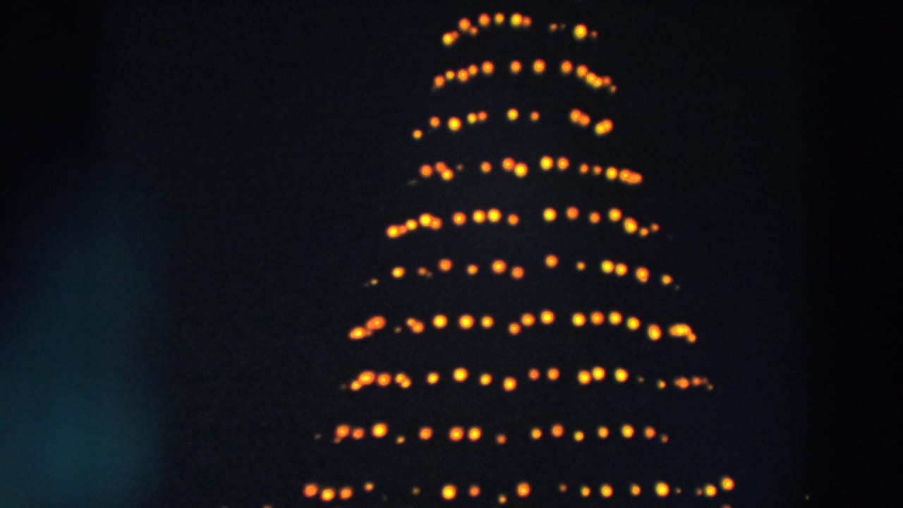 1957 Wheeling, Ohio 8mm frame showing the upper portion of a tall outdoor Christmas tree lit with warm rows of bulbs at night.