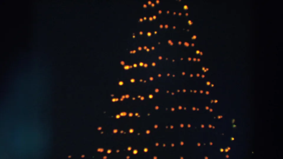 1957 Wheeling, Ohio home-movie frame of a tall Christmas tree light display, with warm bulbs forming horizontal bands in darkness.