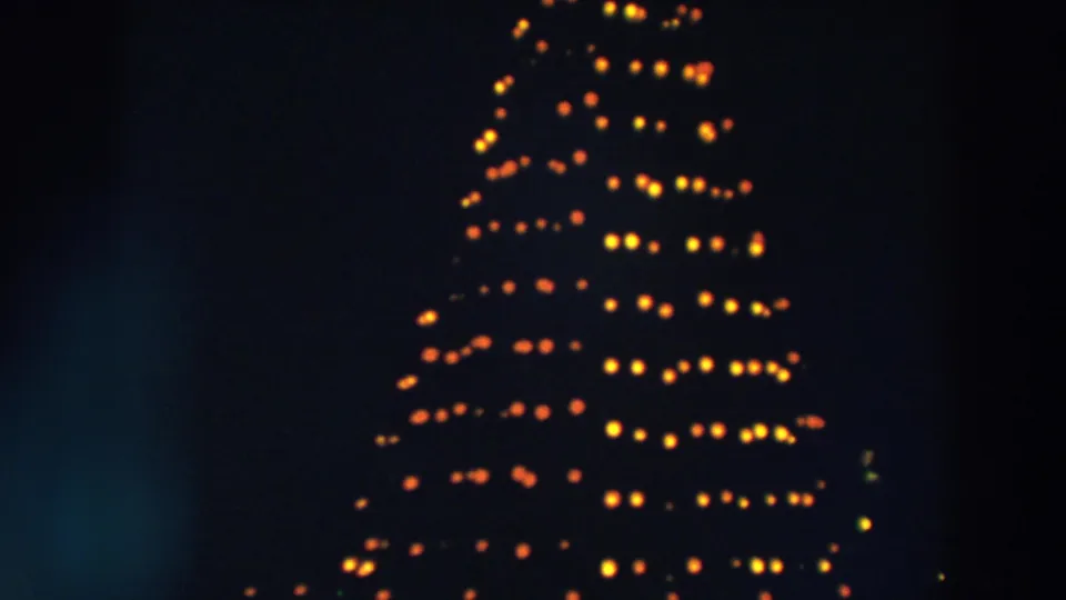 1957 Wheeling, Ohio 8mm frame showing the middle-to-lower portion of a tall Christmas tree with rows of warm holiday lights.