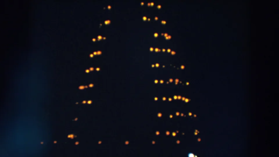 1957 Wheeling, Ohio frame showing the lower rows of a Christmas tree-shaped light installation with warm bulbs in darkness.