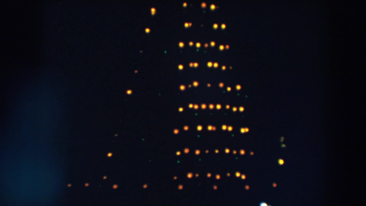 1957 Wheeling, Ohio home-movie frame showing blurred yellow and green lights forming a tall pattern against a dark night sky.