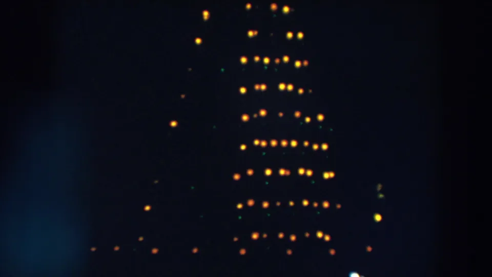 1957 Wheeling, Ohio home-movie frame showing blurred yellow and green lights forming a tall pattern against a dark night sky.