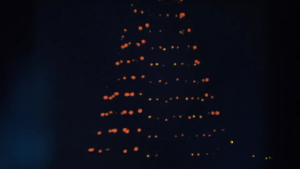 1957 Wheeling, Ohio home-movie frame showing a large outdoor Christmas tree glowing with orange and yellow lights against a dark sky.