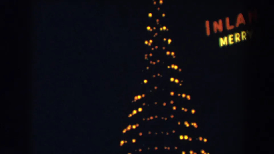 1957 8mm frame with a glowing Christmas tree and partial illuminated sign reading as fragments of holiday wording.