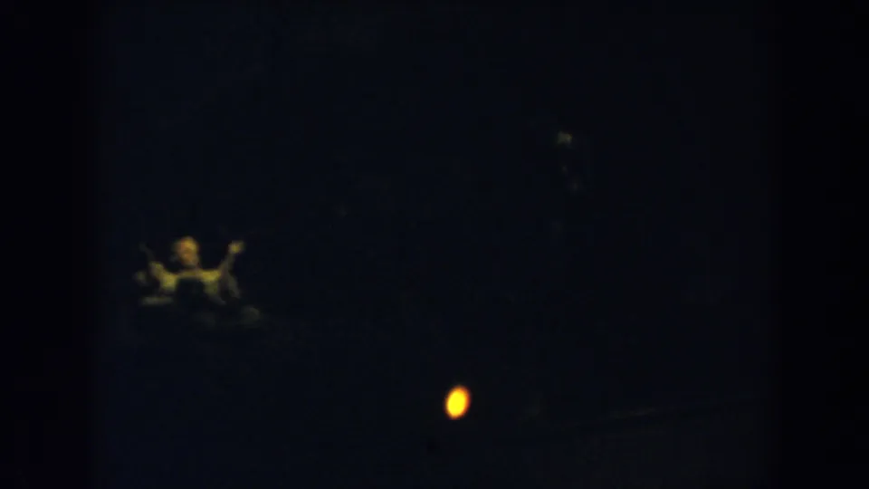 Underexposed 1957 8mm frame from Wheeling, Ohio, with a yellow light and indistinct human presence near the lower edge.