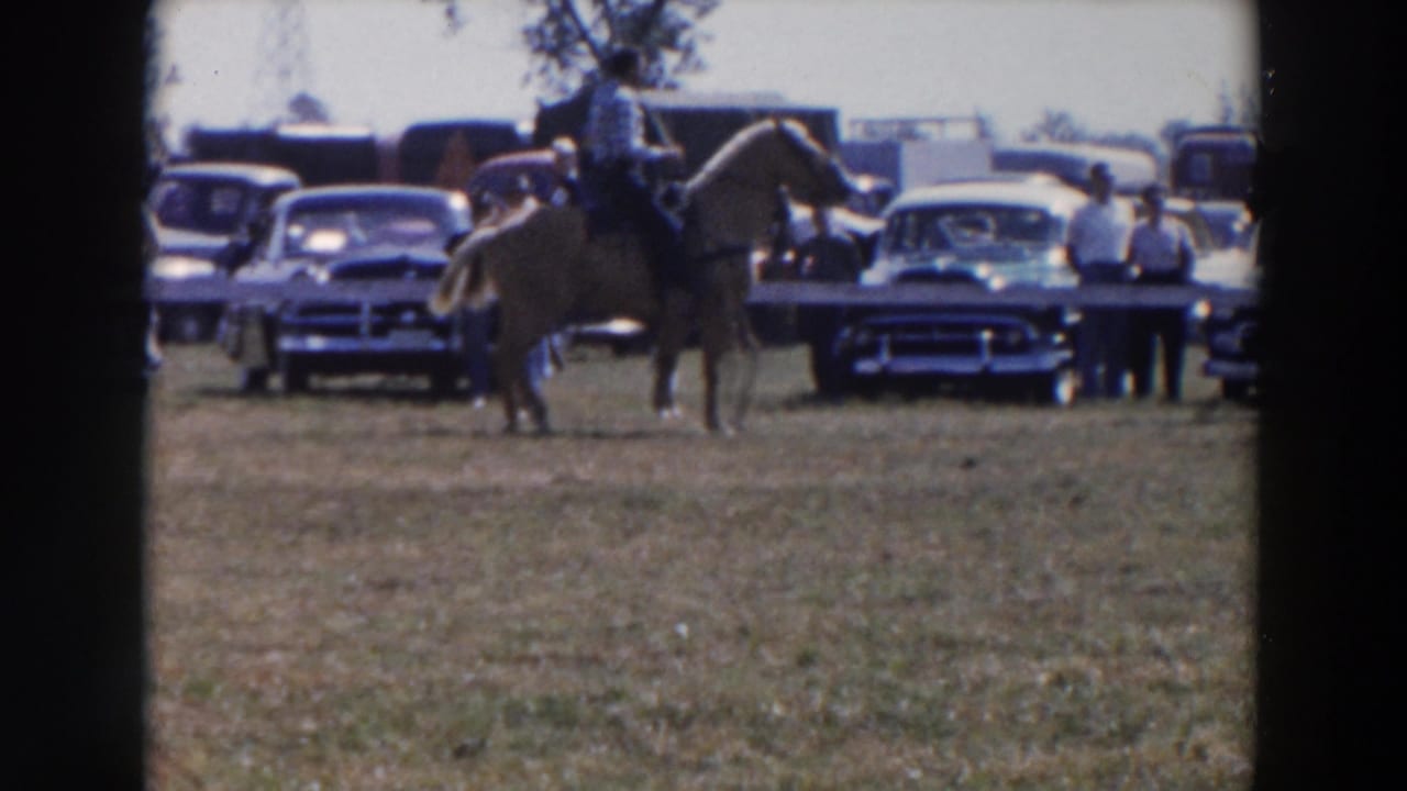 1957 Wheeling, Ohio rodeo footage shows a rider on a light-colored horse moving across grass with mid-century cars and onlookers in back.