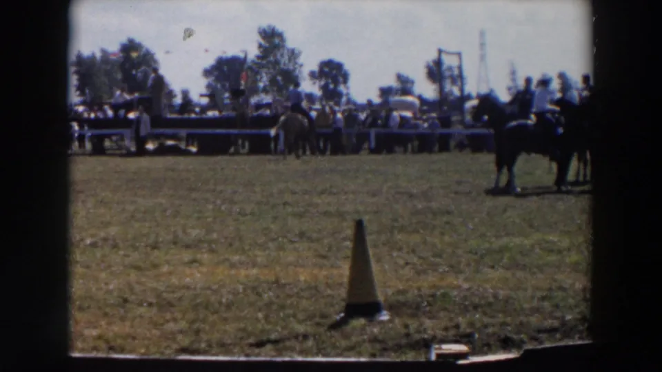 Wide 1957 Wheeling, Ohio rodeo view with riders and horses near a spectator barrier and a traffic cone in the foreground.