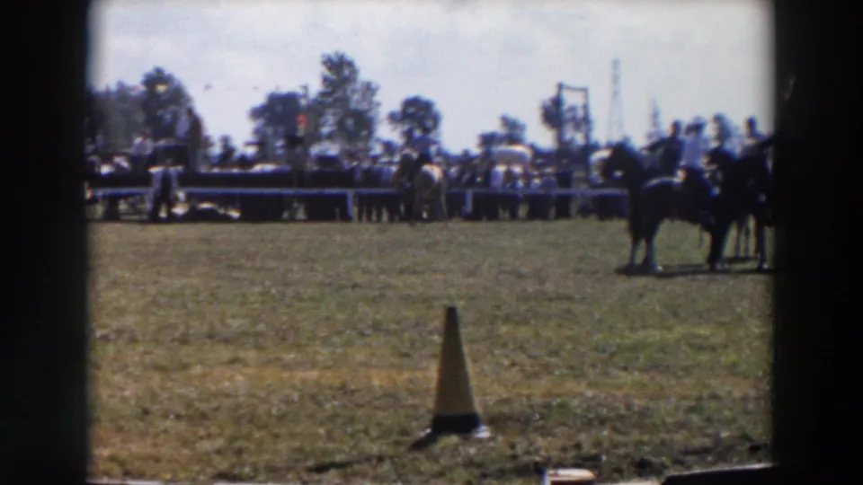 1957 Wheeling, Ohio home-movie frame shows riders on horseback near a crowd line, with an orange and black cone on the grass.