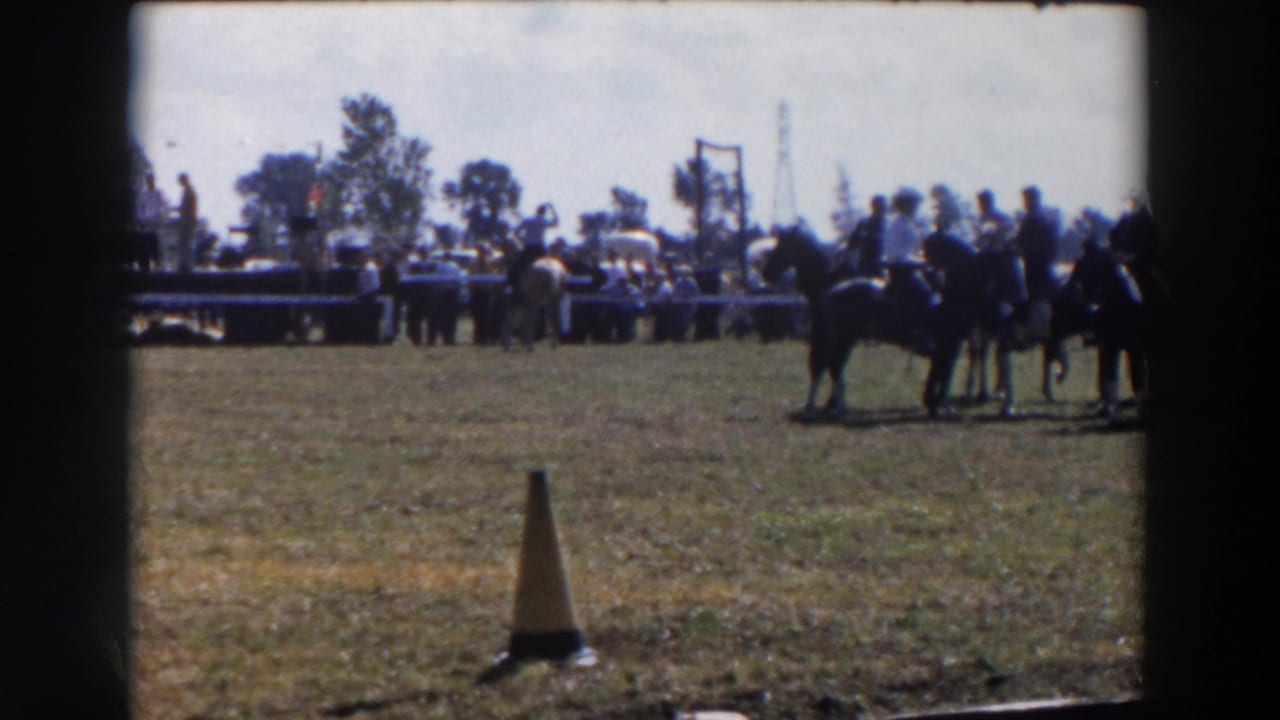 In 1957 Wheeling, Ohio footage, riders on horseback wait in a grassy show ring as spectators and tables sit in the background.