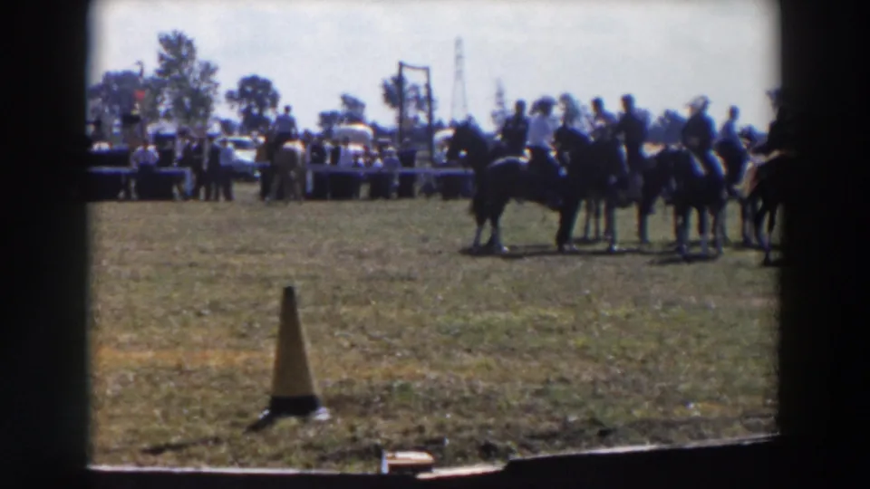 Riders on horseback cluster on the right side of a Wheeling, Ohio show ring while people and vehicles line the background.
