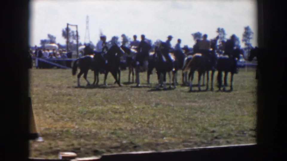 1957 Wheeling, Ohio 8mm frame showing riders on horseback grouped in a grassy show ring with spectators and classic cars in the background.