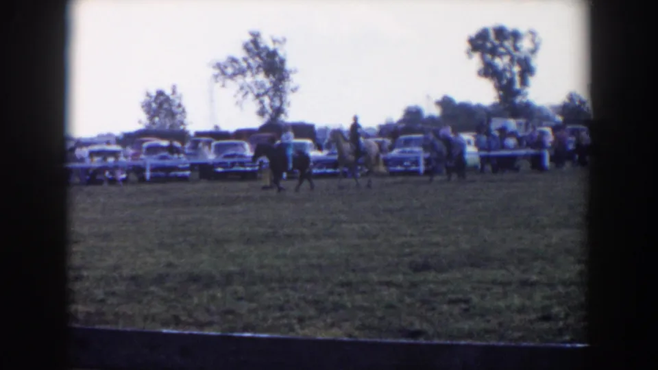 1957 Wheeling, Ohio 8mm frame with a rider on a light-colored horse in the ring and spectators near parked cars behind.