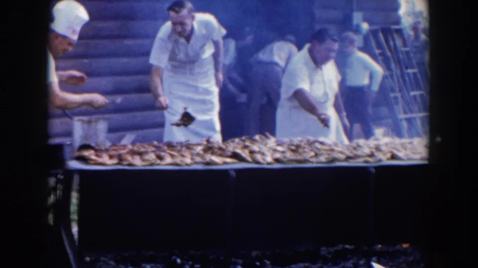 Men in white cook uniforms and aprons work over rows of fish on an outdoor grill during the Wheeling, Ohio gathering.
