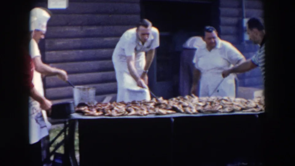 Cooks in white hats and aprons work over a long barbecue table during an outdoor gathering in Wheeling, Ohio, based on clip metadata.