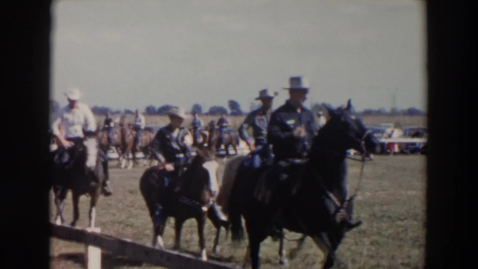 1957 Wheeling, Ohio county fair footage shows several riders on horseback moving across a grassy field with spectators and parked cars in the background.