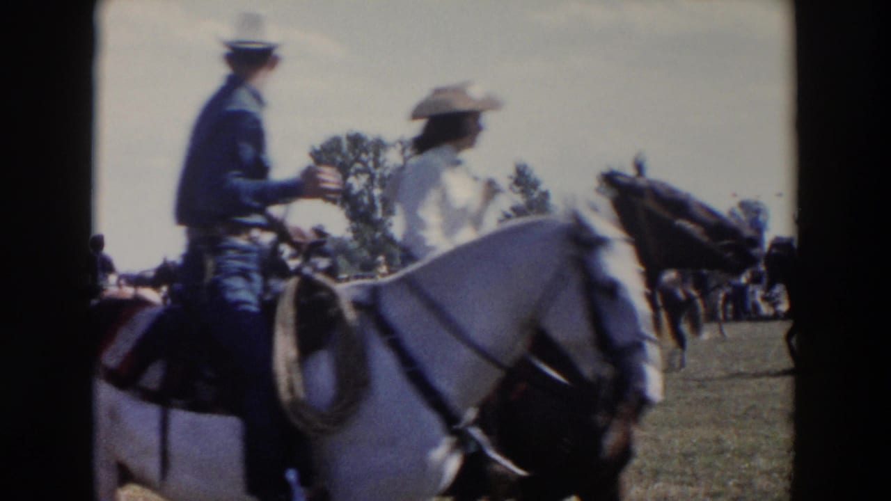1957 Wheeling, Ohio home-movie frame showing riders on horseback passing close to the camera during a rodeo parade on grass.