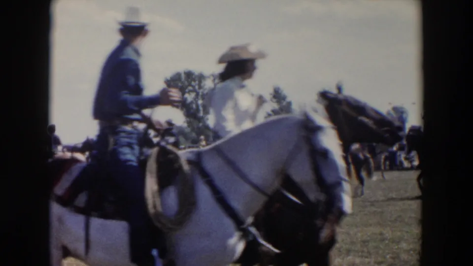 1957 Wheeling, Ohio home-movie frame showing riders on horseback passing close to the camera during a rodeo parade on grass.