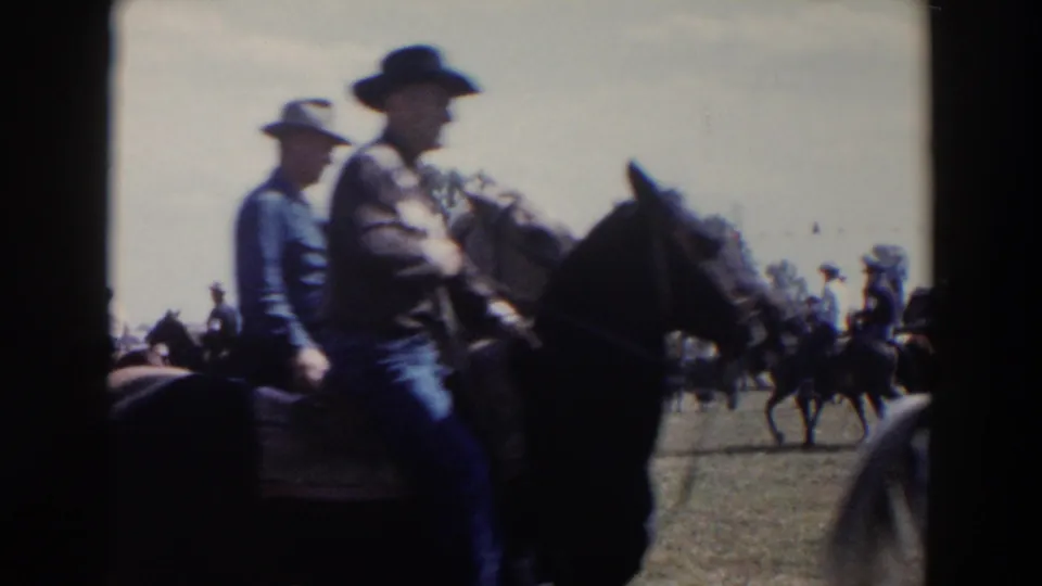 Mounted cowboys in hats ride through the 1957 Wheeling, Ohio rodeo parade, with other horses and spectators farther back.