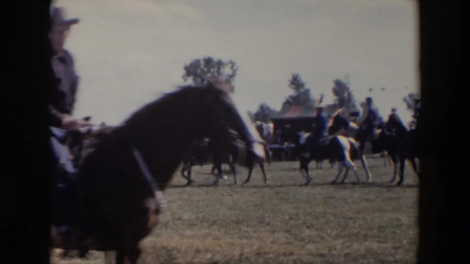 1957 Wheeling, Ohio home-movie frame showing horseback riders crossing an open field during a public event.