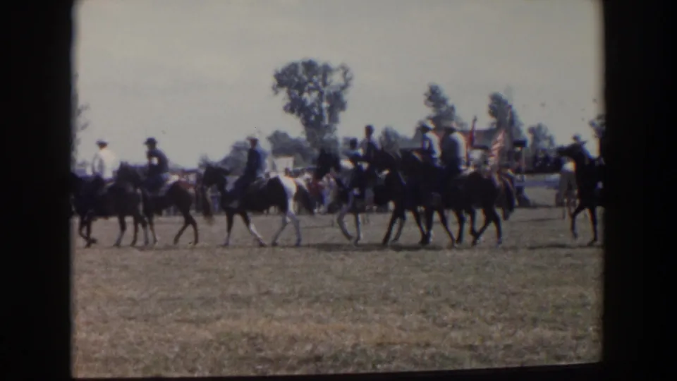Home-movie frame of riders in cowboy hats moving in formation across a grassy field in Wheeling, Ohio, 1957.