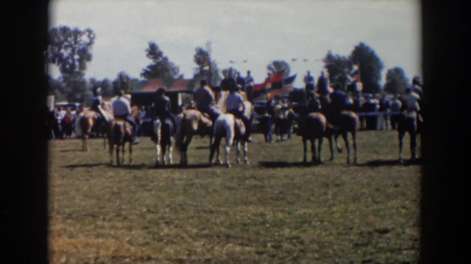 Several riders pause or gather on horseback at a 1957 Wheeling, Ohio outdoor event, with spectators and flags beyond them.